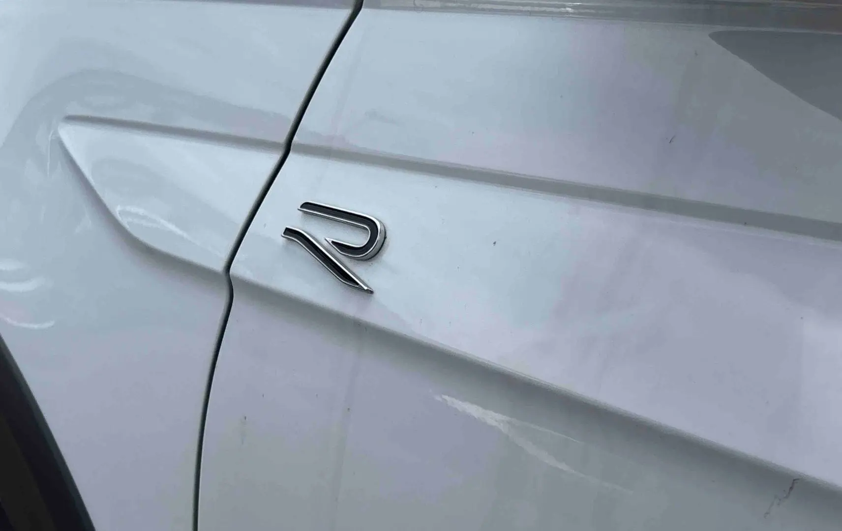 Détail du logo R sur la porte côté gauche d’un Volkswagen Taigo blanc, soulignant la finition R-Line.