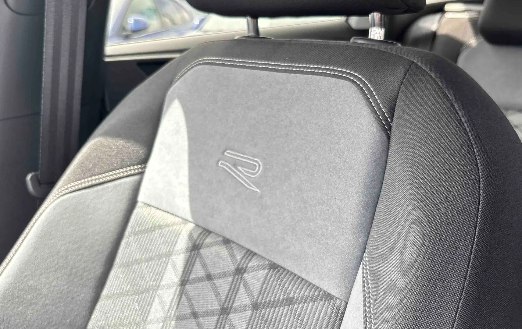Gros plan sur le siège avant gris foncé avec logo R-Line embossé, coutures blanches et motif géométrique.