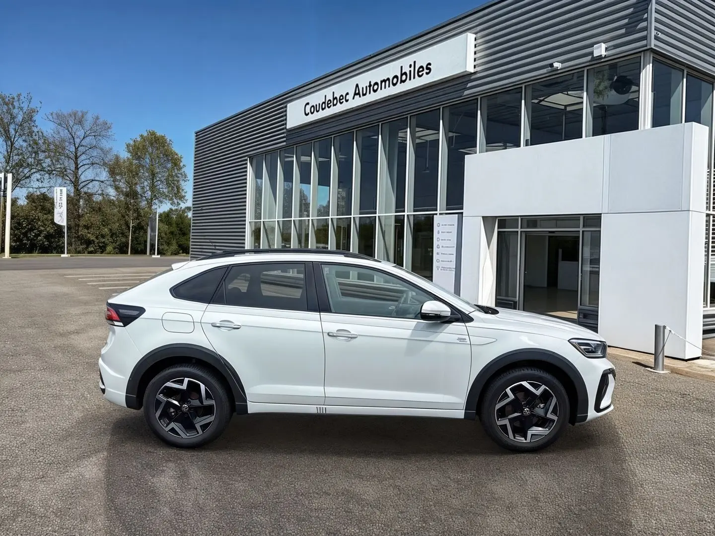 Profil droit du Volkswagen Taigo blanc 2025 avec jantes alliage noires et détails R-Line devant un concessionnaire.