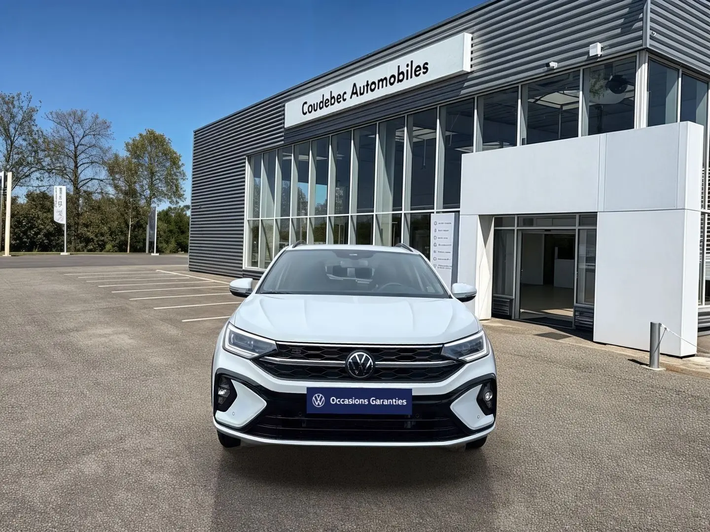 Vue de face du Volkswagen Taigo blanc 2025 avec calandre R-Line et projecteurs Matrix LED devant un concessionnaire.
