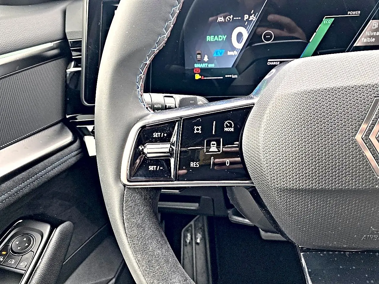 Gros plan sur le volant gris et les commandes multifonctions du Renault Austral 1.2 e-tech hybride, tableau de bord digital en arrière-plan.