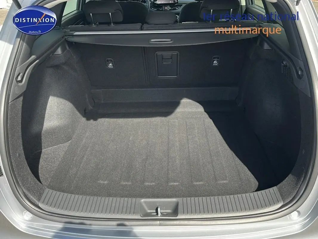 Coffre ouvert d'une Hyundai i30 SW gris clair, vue arrière montrant l'espace de chargement et la plage arrière.