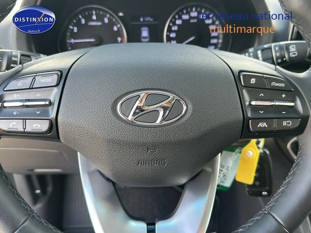 Vue rapprochée du volant noir de la Hyundai i30 SW 2022 avec commandes intégrées et logo central chromé.