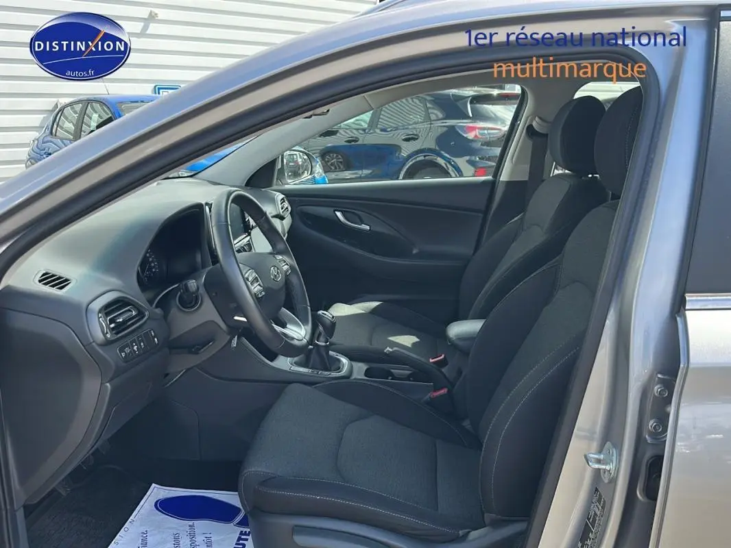 Intérieur de la Hyundai i30 SW gris clair 2022, vue côté conducteur avec sièges noirs et volant multifonction.