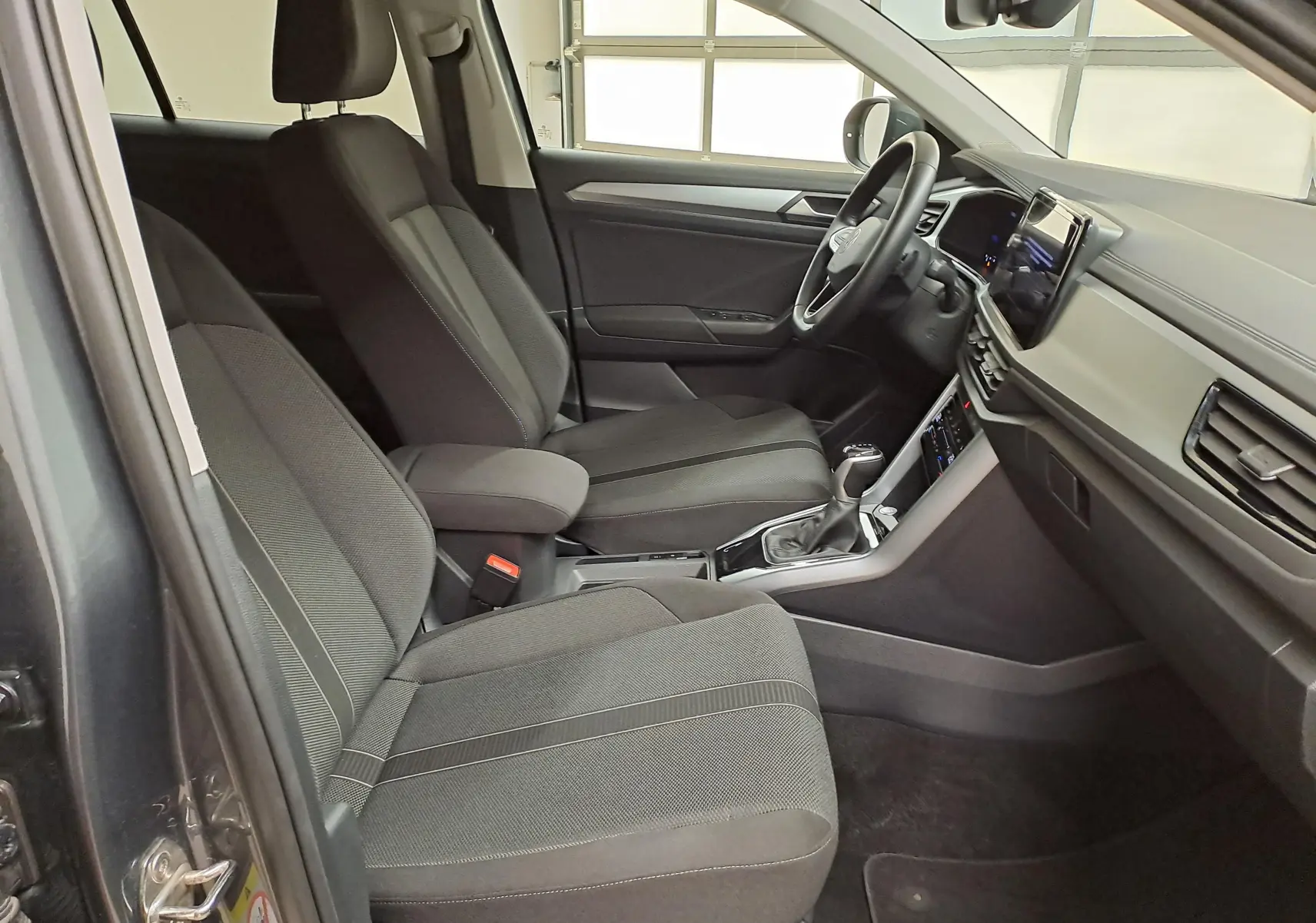 Intérieur avant droit du Volkswagen T-Roc 2024 gris Indium, montrant sièges tissu et tableau de bord moderne.