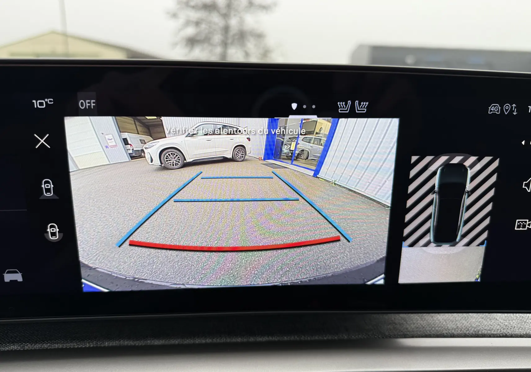 Vue caméra de recul montrant un SUV blanc Okenite Peugeot 3008 hybride garé près d'un bâtiment avec toit noir visible.