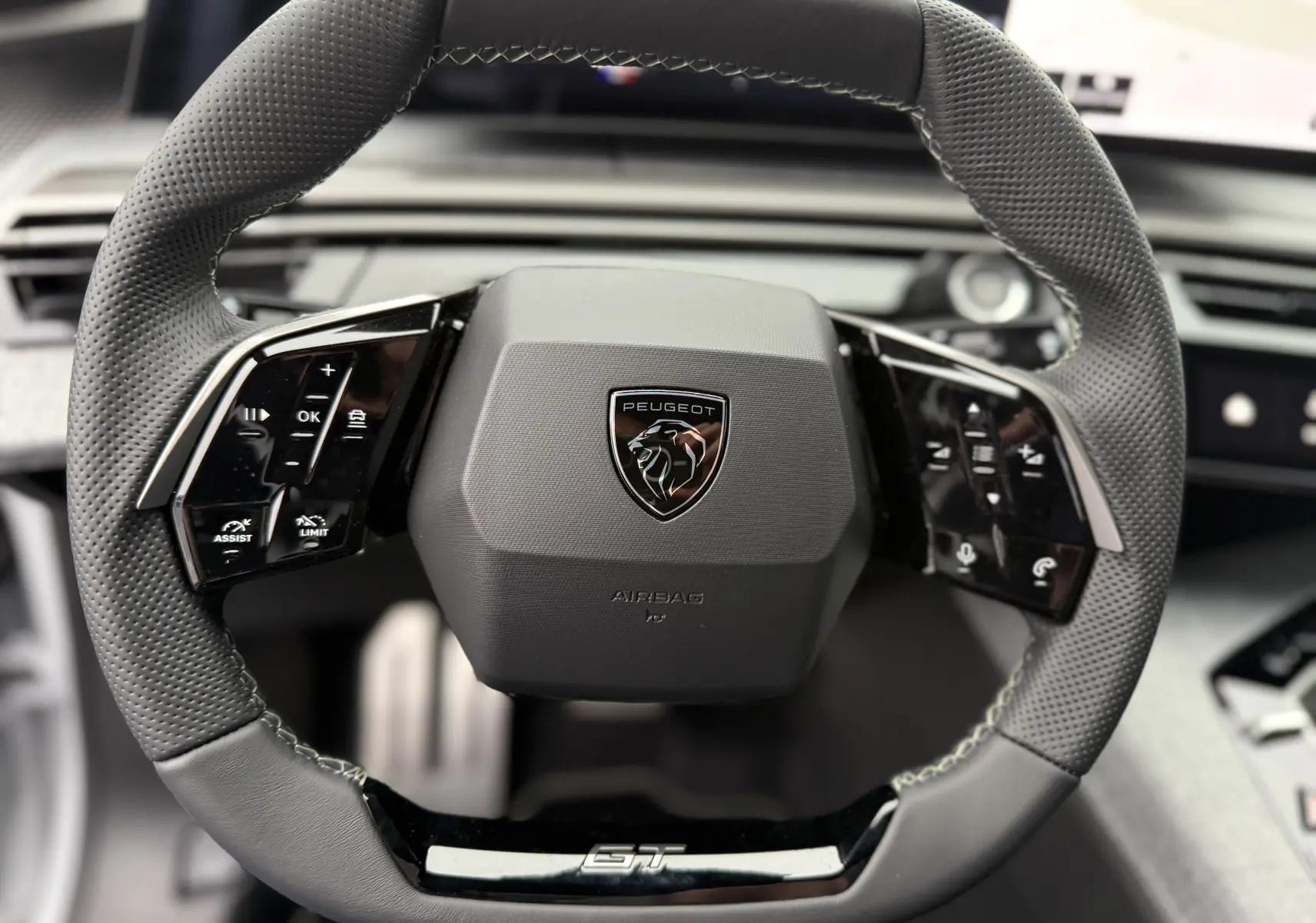Gros plan sur le volant multifonction en cuir perforé noir du Peugeot 3008 Hybrid 2025 avec logo central et badge GT.
