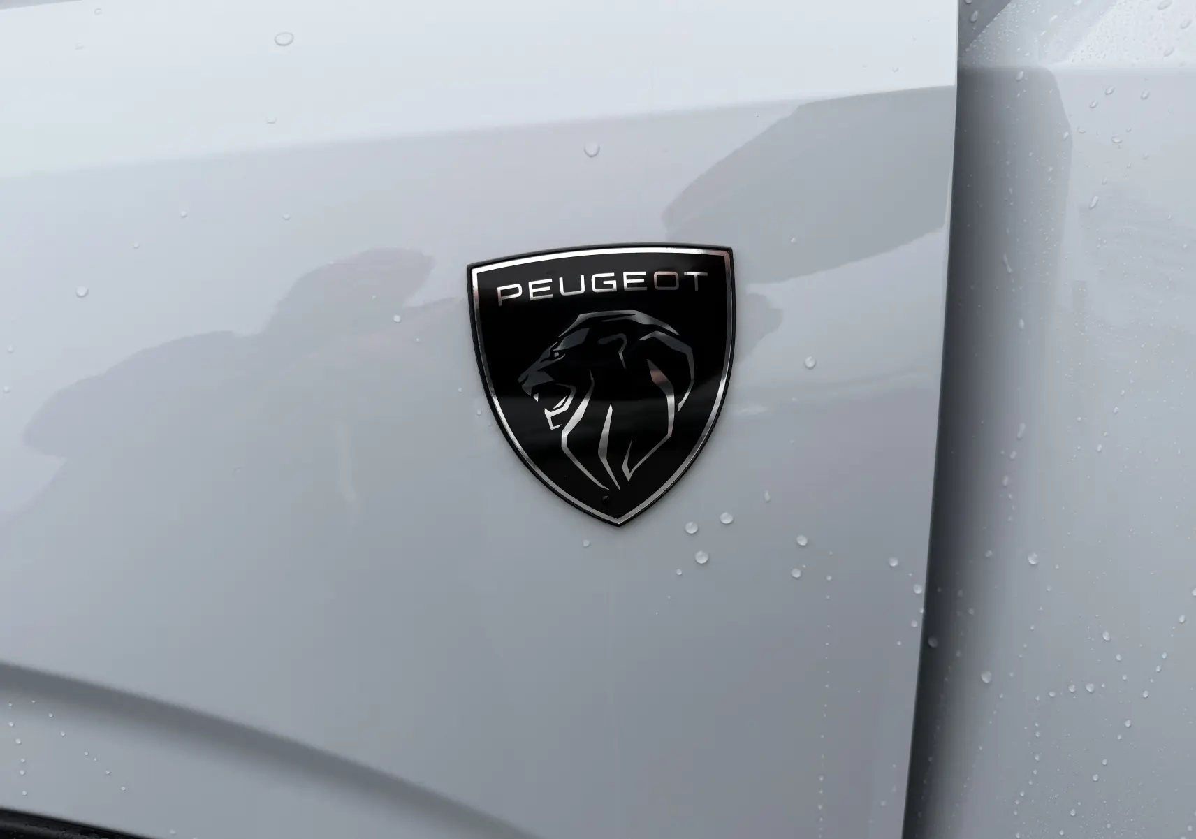 Gros plan sur l'écusson noir Peugeot sur la carrosserie blanche Okenite du SUV 3008 Hybrid 2025.