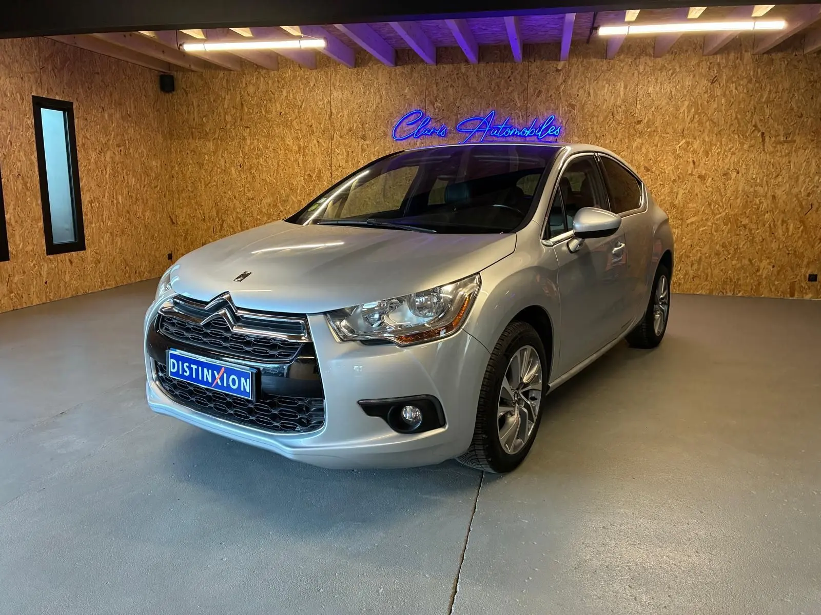 Vue 3/4 avant d'une DS4 gris clair, avec calandre chromée et jantes alliage dans un showroom au mur bois.