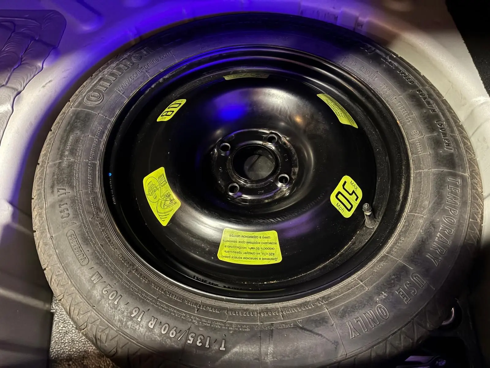 Gros plan sur la roue de secours noire avec étiquettes jaunes dans le coffre d'une DS4 gris 2014.