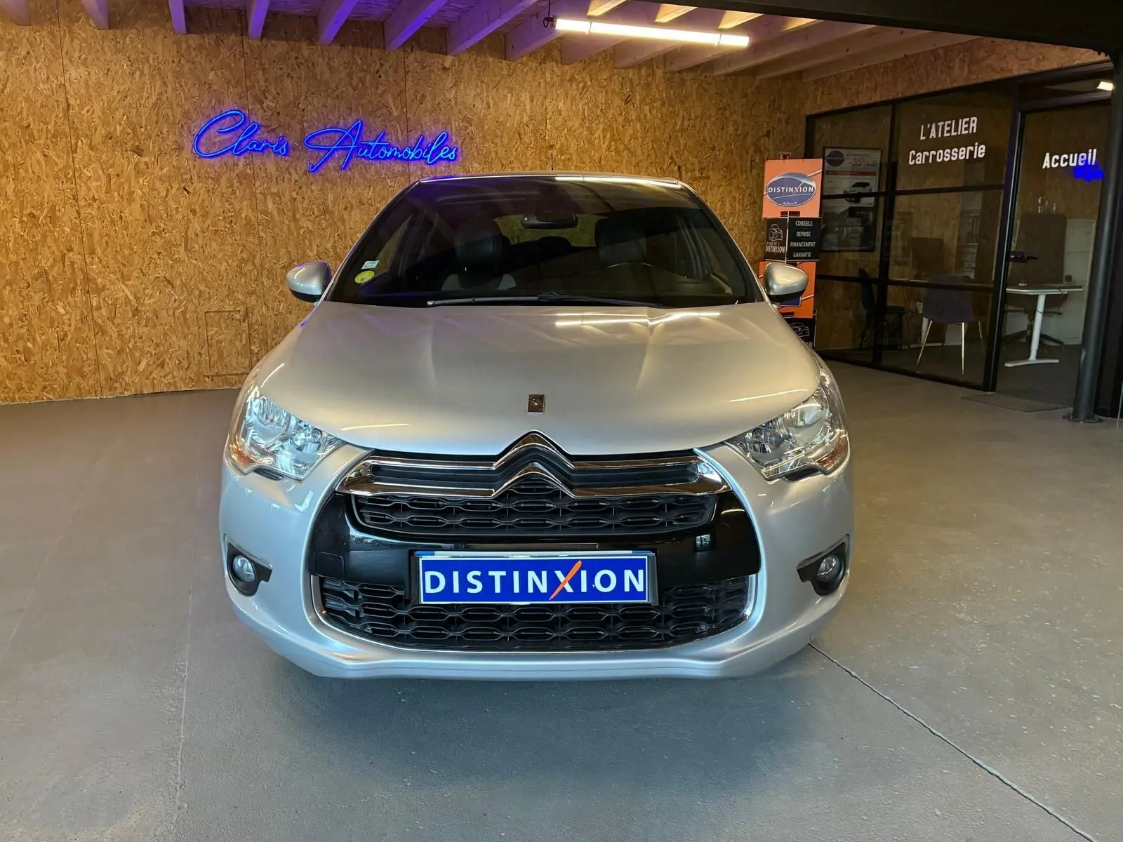 Vue avant d'une DS4 gris clair diesel de 2014, avec calandre noire et logo Citroën, en intérieur showroom.