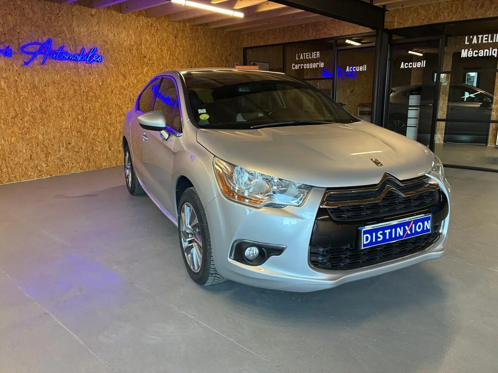 Vue 3/4 avant droite d'une DS4 gris clair diesel de 2014, avec calandre noire et phares distinctifs, en intérieur showroom.