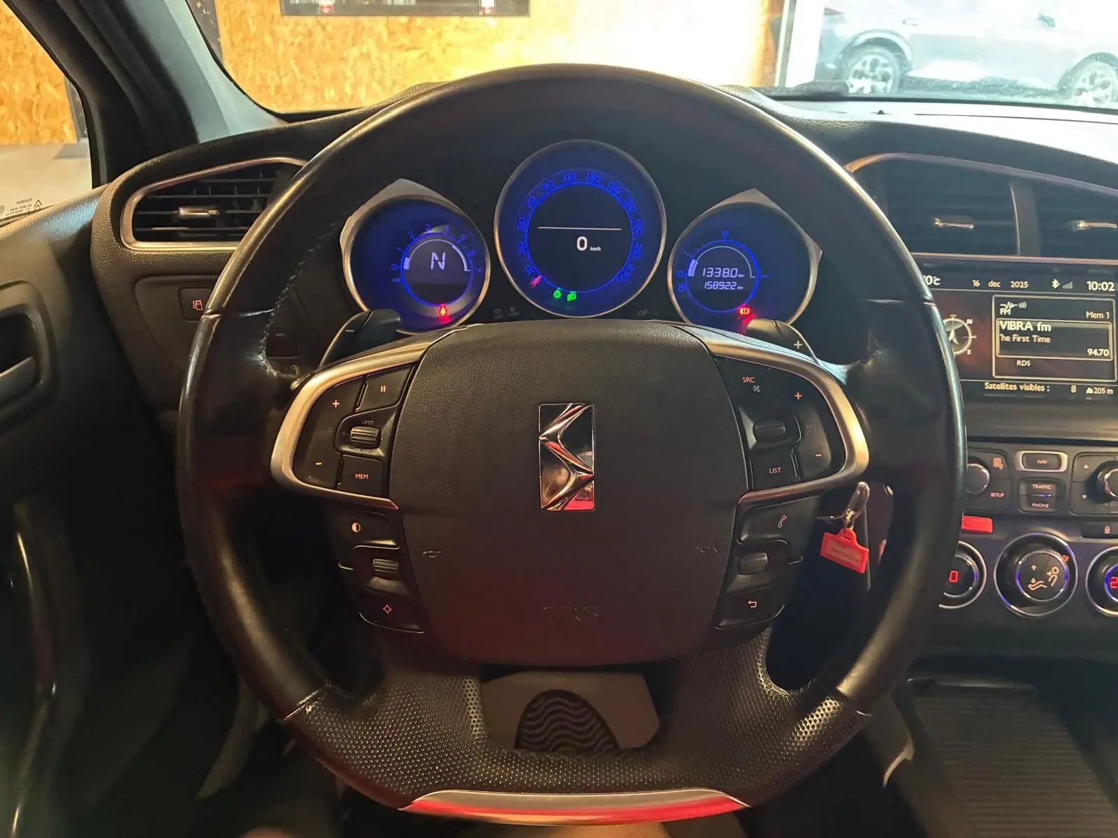 Vue intérieure centrée sur le volant noir du DS4 gris, avec tableau de bord et compteurs lumineux bleus en arrière-plan.