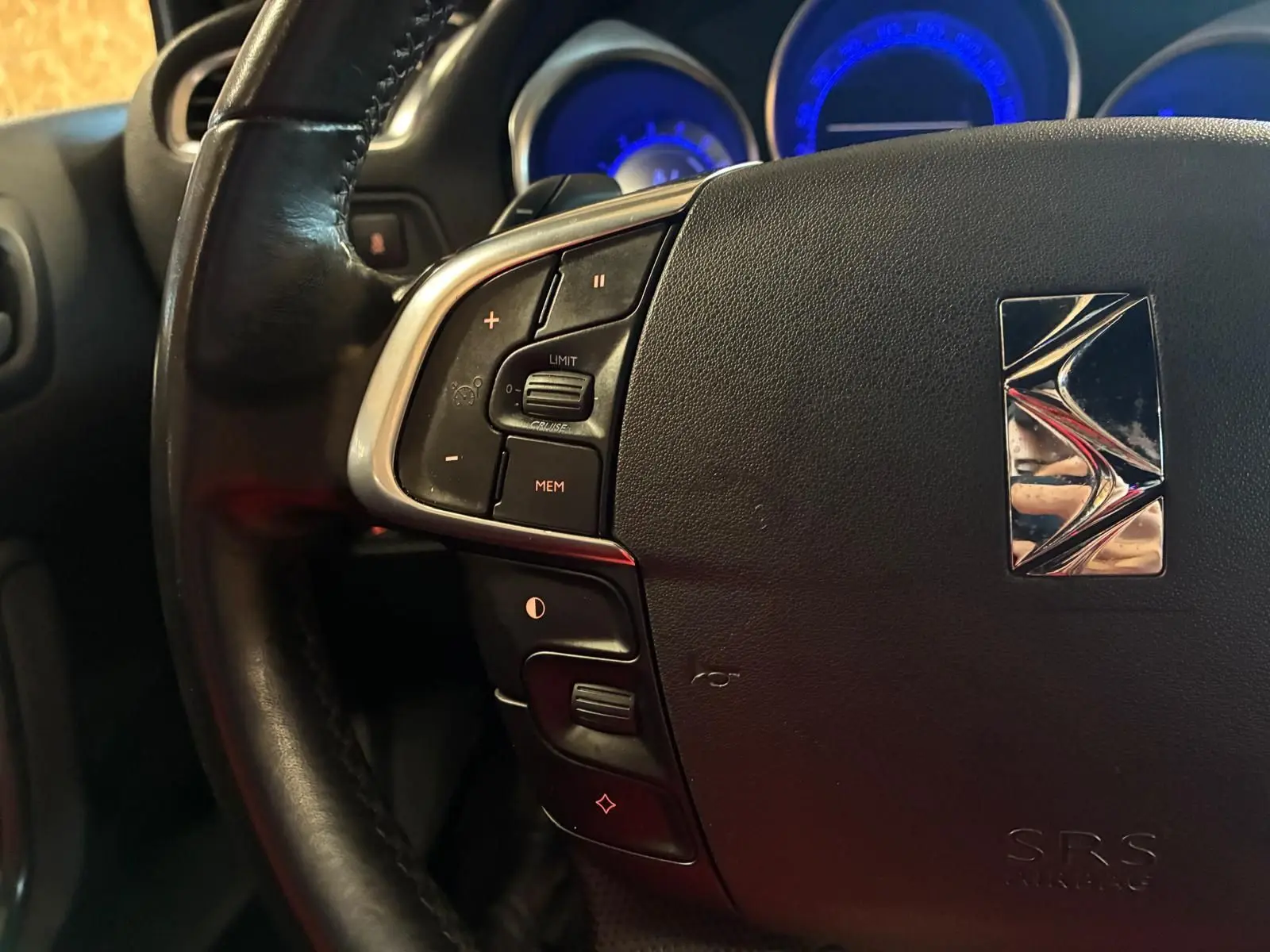 Gros plan sur le volant noir de la DS4 2014 avec commandes intégrées et tableau de bord éclairé en bleu.