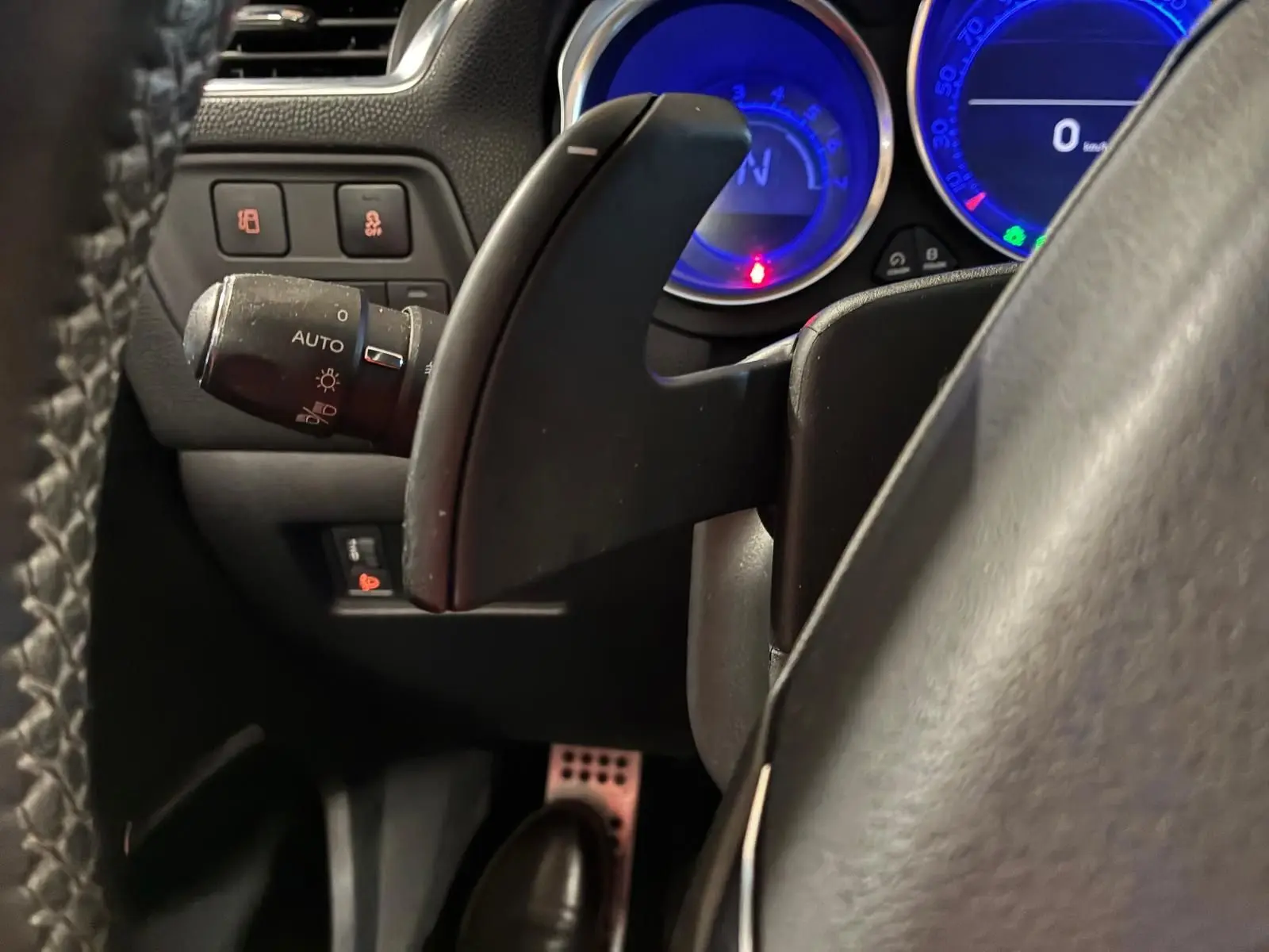 Gros plan sur la palette de changement de vitesse côté droit du volant d’un DS4 gris, avec compteurs bleus en arrière-plan.