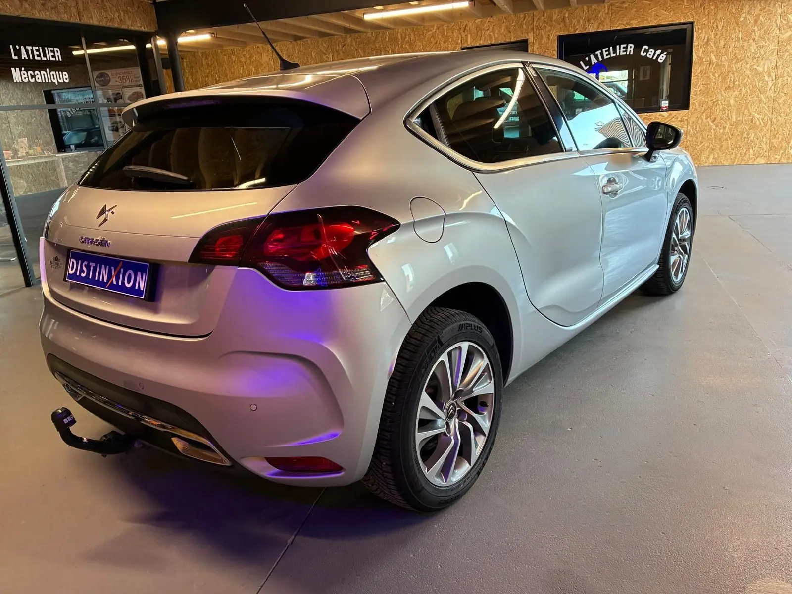 Vue 3/4 arrière droite d'une DS4 gris clair avec hayon, jantes alliage et attelage dans un garage intérieur.