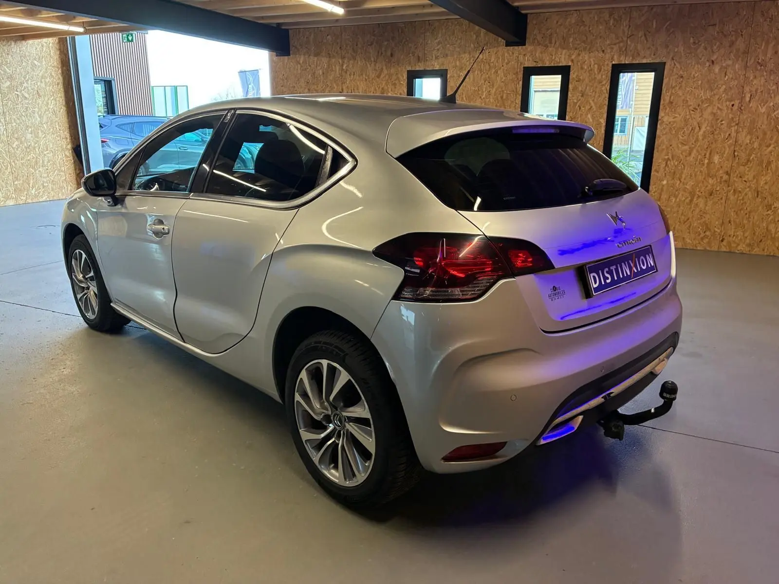 Vue 3/4 arrière droite d'une DS4 gris métallisé avec hayon, feux arrière LED et attelage visible en intérieur lumineux.