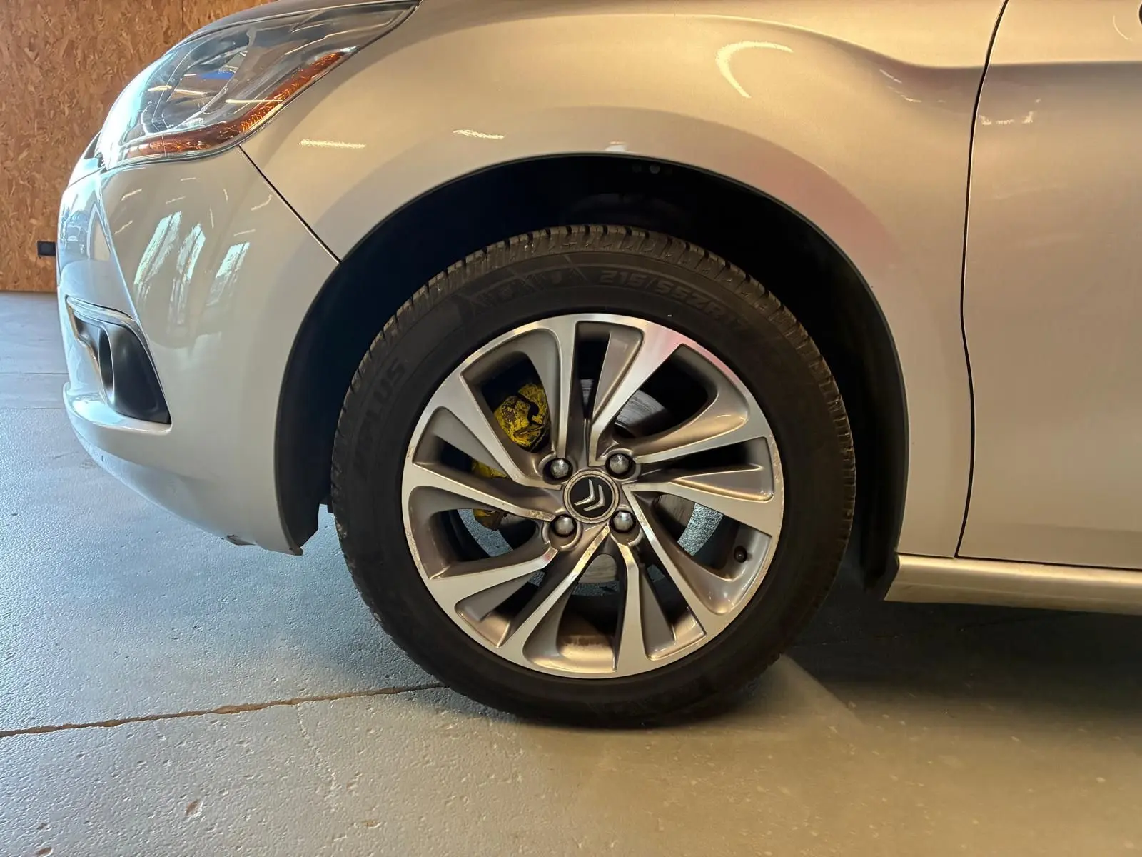 Gros plan sur la roue avant gauche d'une DS4 gris clair, mettant en valeur la jante alliage et l'étrier de frein jaune.