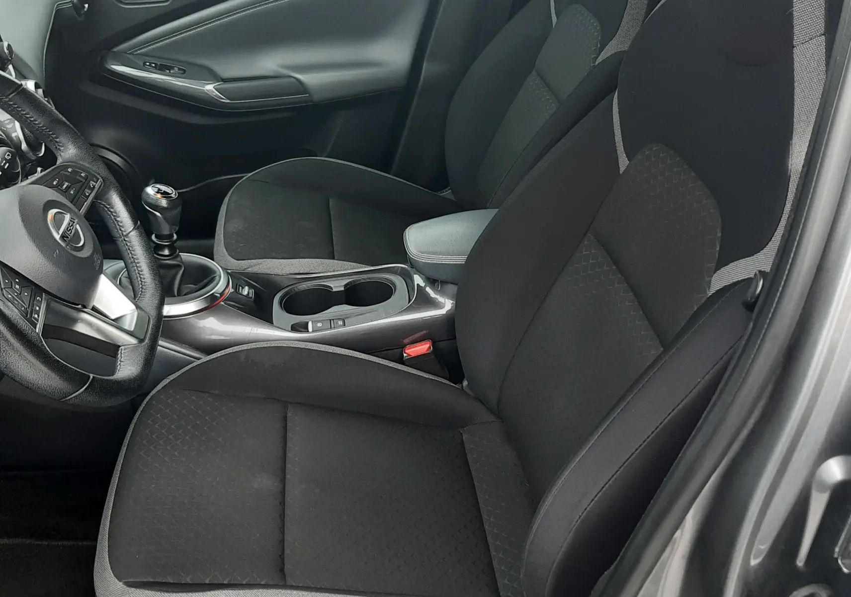 Vue intérieure côté conducteur du Nissan Juke gris 2020, montrant sièges tissu noirs et levier de vitesse manuel.
