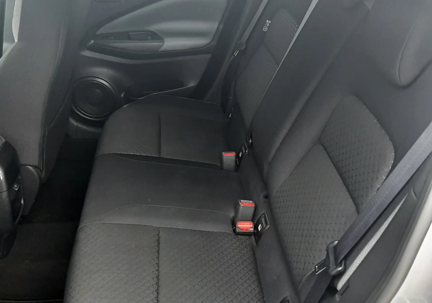 Vue latérale droite de la banquette arrière noire en tissu du Nissan Juke gris, avec ceintures de sécurité visibles.