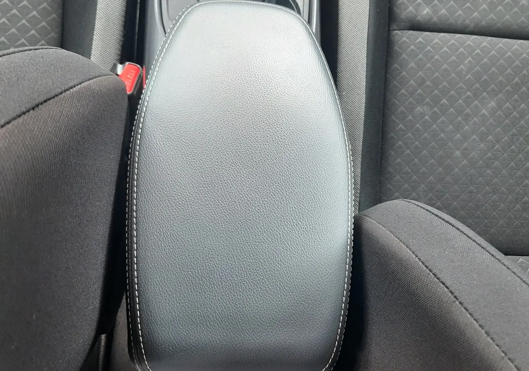 Vue plongeante sur l'accoudoir central noir et les sièges en tissu gris du Nissan Juke 2020 intérieur.