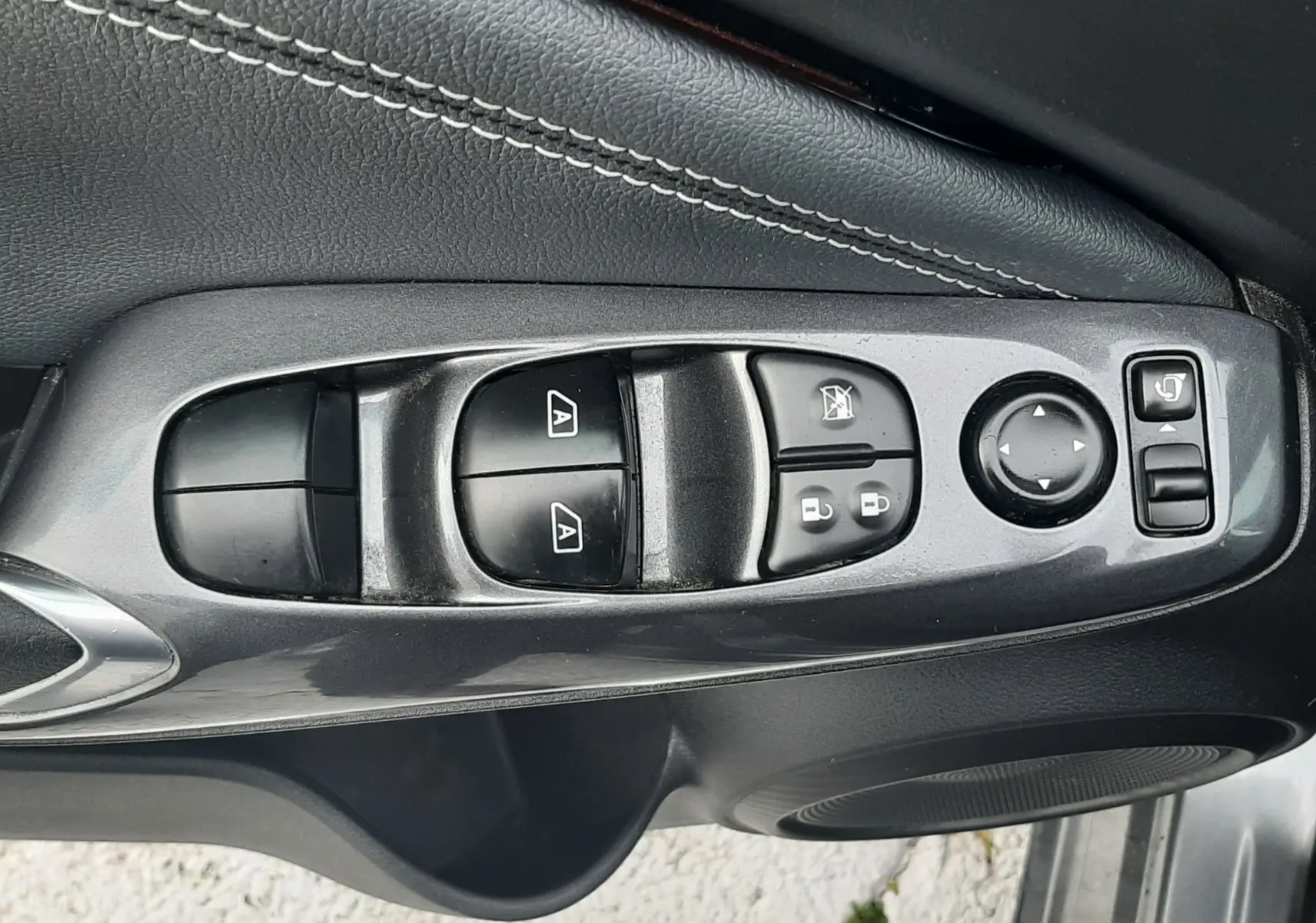 Gros plan sur la commande des vitres et rétroviseurs côté conducteur du Nissan Juke gris, avec surpiqûres blanches visibles.