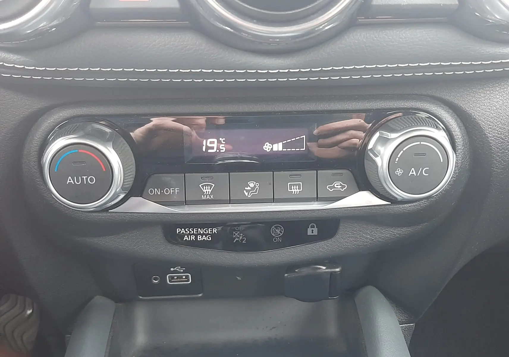 Vue rapprochée du tableau de bord noir du Nissan Juke 2020, mettant en valeur la commande de climatisation digitale à 19,5°C.