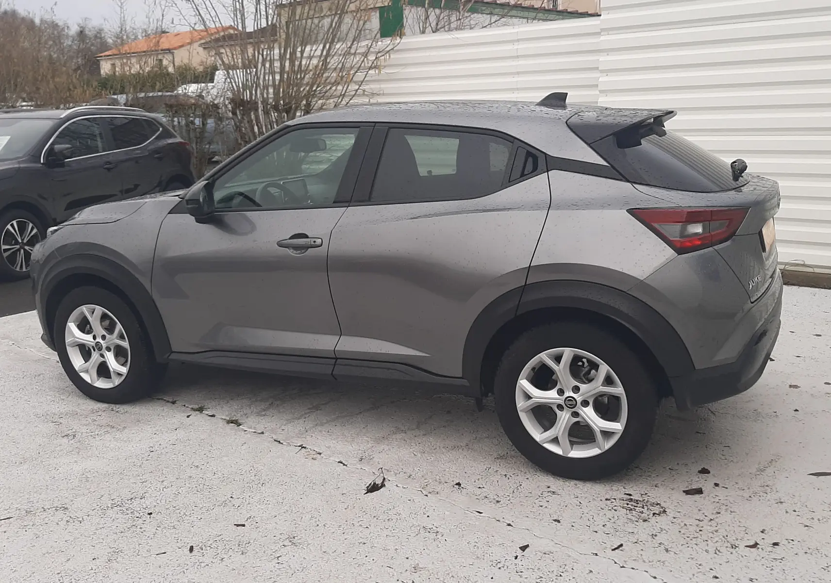 Nissan Juke gris vu de profil côté gauche, SUV compact avec jantes alliage et vitres teintées.