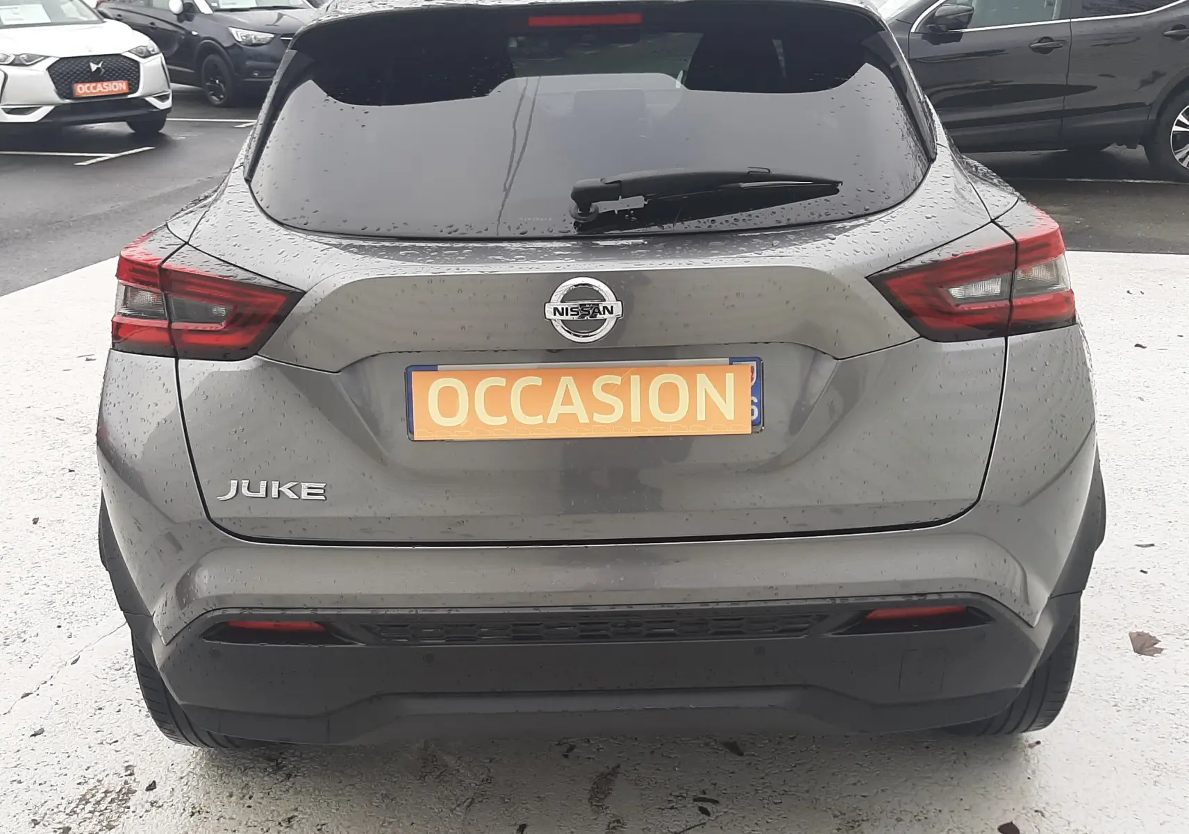 Vue arrière d'un Nissan Juke gris 2020 avec feux arrière LED et plaque "OCCASION" sur un parking.