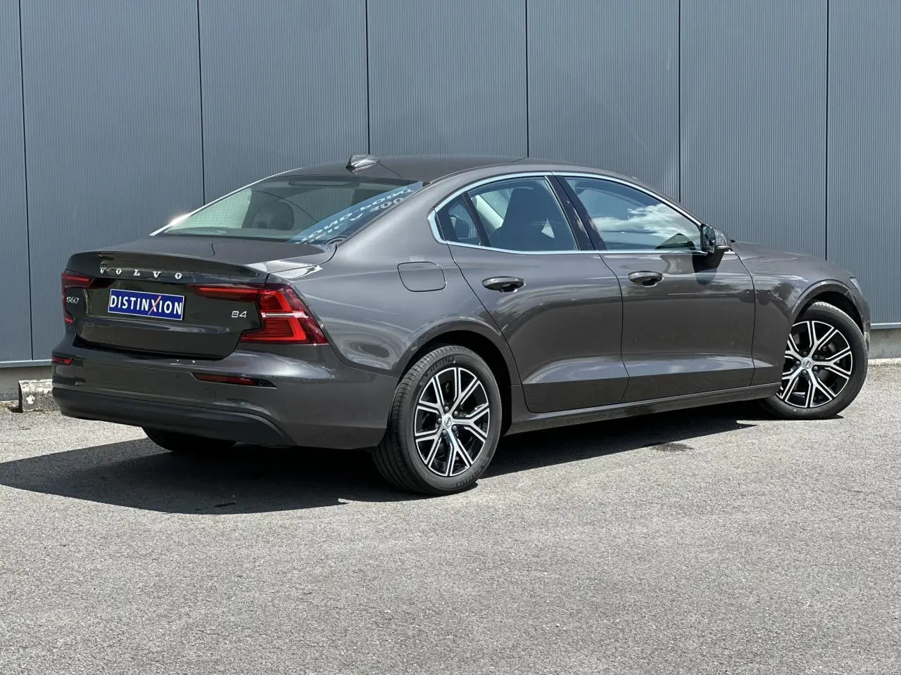 Volvo S60 B4 gris Platinium vue 3/4 arrière droit, jantes alliage noires et feux arrière LED distinctifs.