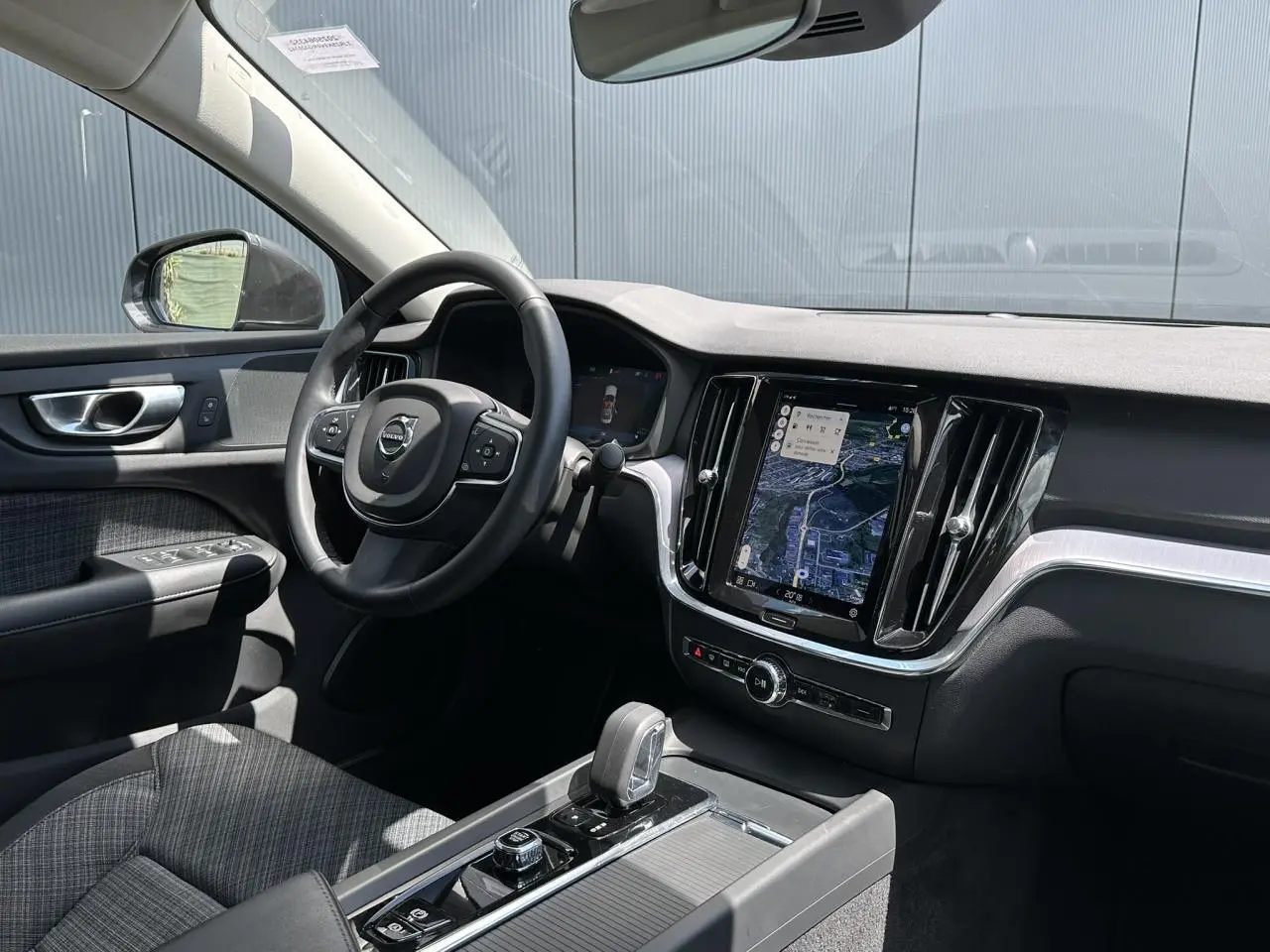 Intérieur avant droit du Volvo S60 2024 avec tableau de bord noir, écran tactile vertical et volant multifonction.