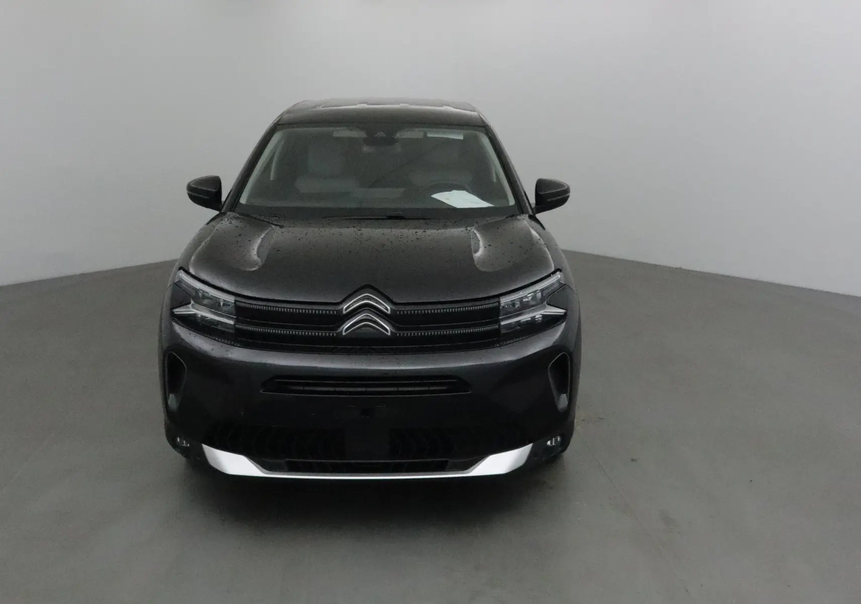 Vue frontale d'un Citroën C5 Aircross noir 2024 avec capot légèrement mouillé et calandre distinctive double chevron.