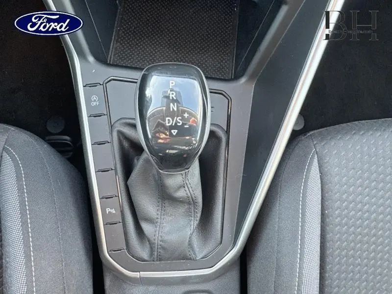 Le levier de vitesses automatique noir au centre de la console d'une Volkswagen Taigo blanc pur, entouré de sièges en tissu gris.