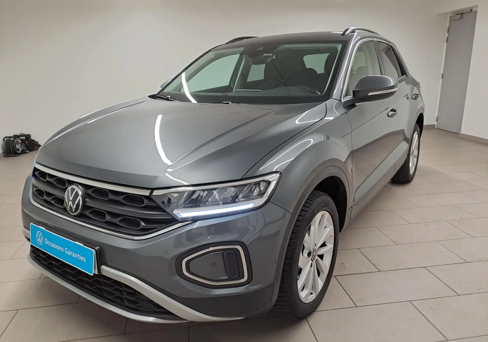 Volkswagen T-Roc 1.5 TSI gris Indium en vue 3/4 avant droit, avec jantes alliage 17'' Johannesburg et feux LED allumés.