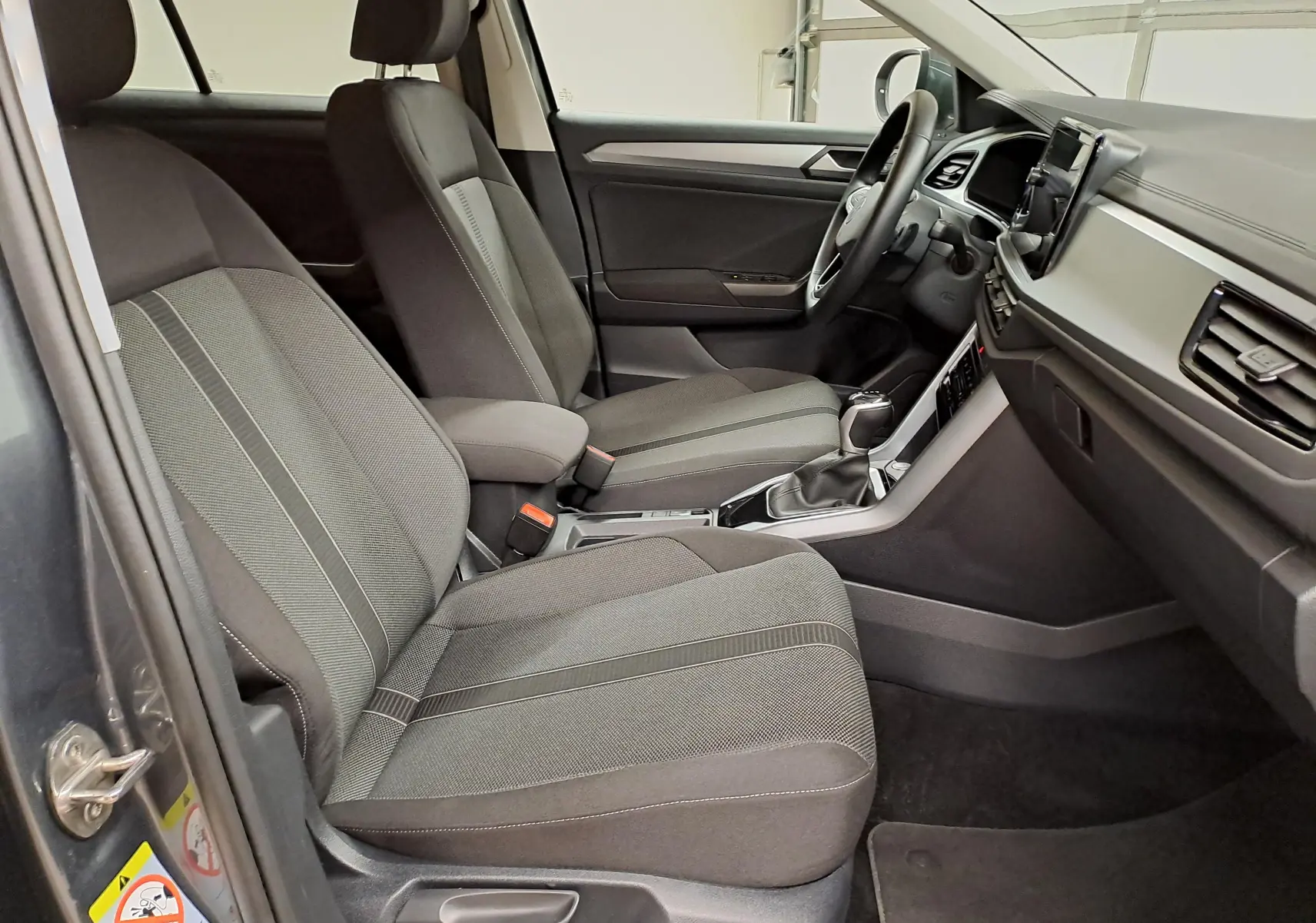 Intérieur avant droit du Volkswagen T-Roc 2024, sièges tissu gris et console centrale avec boîte automatique.