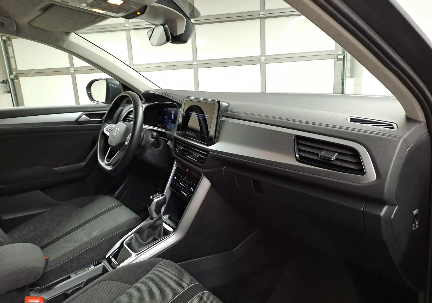 Vue intérieure côté conducteur du Volkswagen T-Roc 1.5 TSI 2024, tableau de bord moderne et écran tactile central.