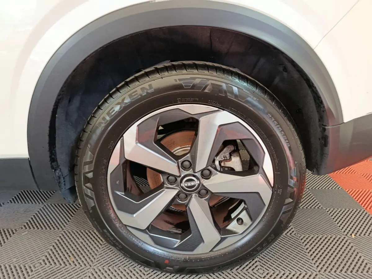 Gros plan sur la roue avant droite du Nissan Qashqai blanc, jante alliage au design moderne et pneu Nexen visible.