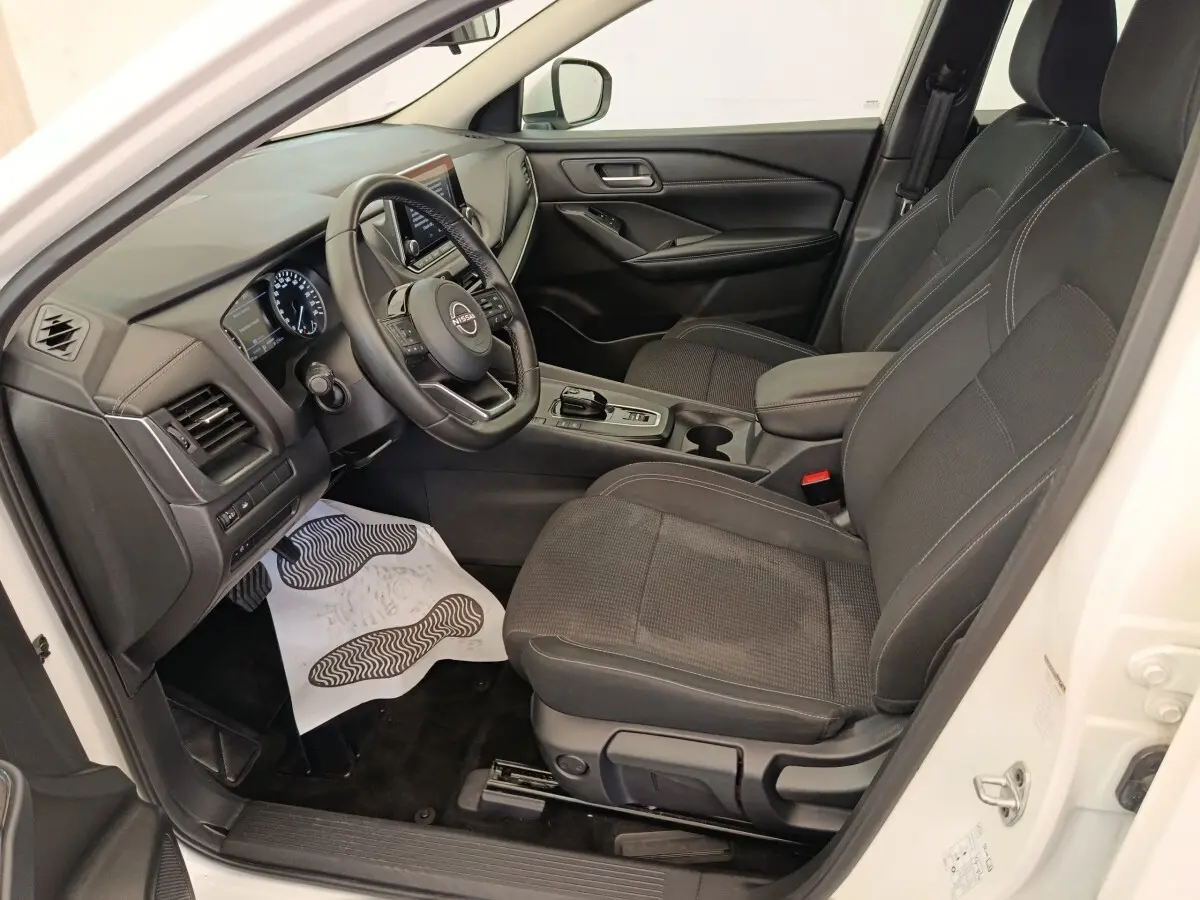 Intérieur avant droit du Nissan Qashqai blanc 2024, avec sièges noirs, volant multifonctions et console centrale moderne.