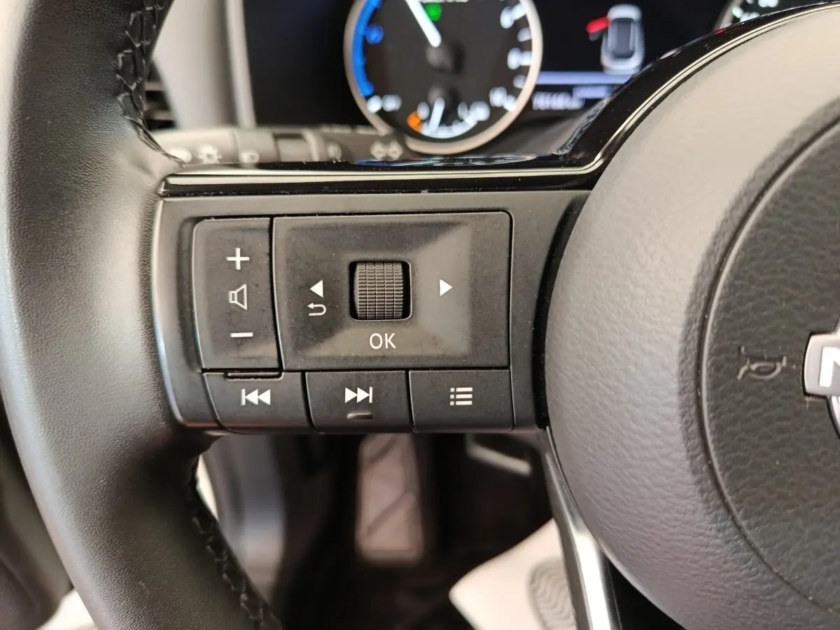 Gros plan sur les commandes gauche du volant noir du Nissan Qashqai e-Power 2024 avec tableau de bord partiellement visible.