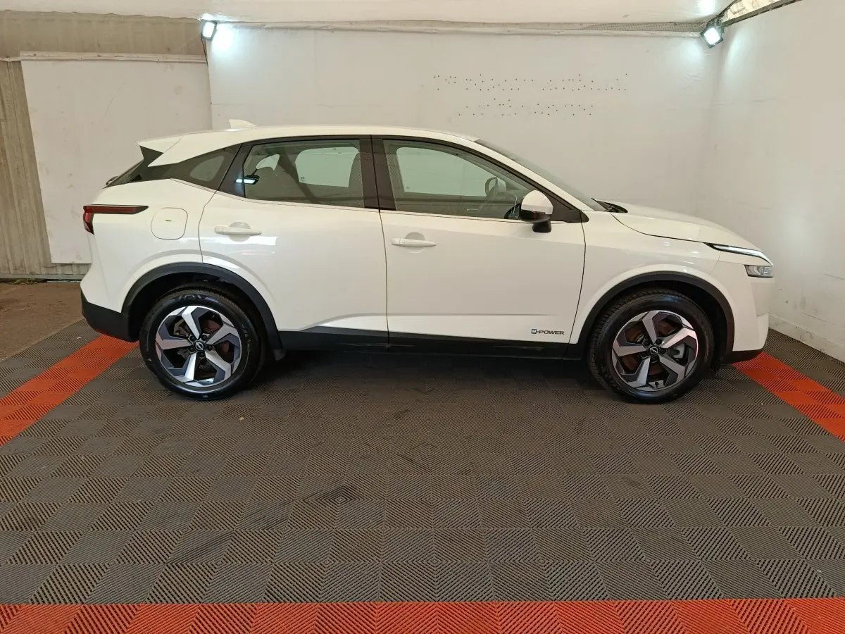 Vue de profil côté gauche d'un Nissan Qashqai e-Power blanc avec jantes alliage et toit noir dans un garage.