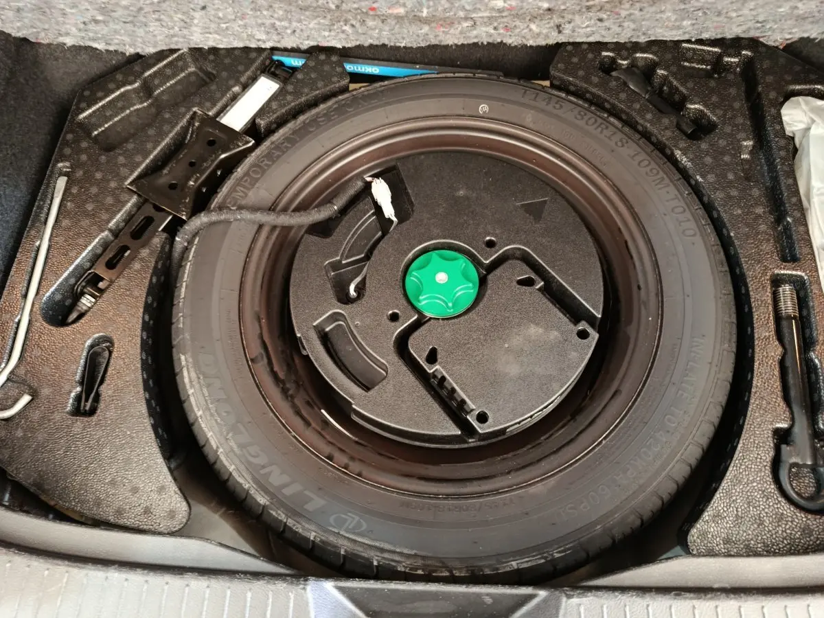 Vue plongeante sur la roue galette noire et ses outils de secours dans le coffre du Nissan Qashqai blanc 2024.