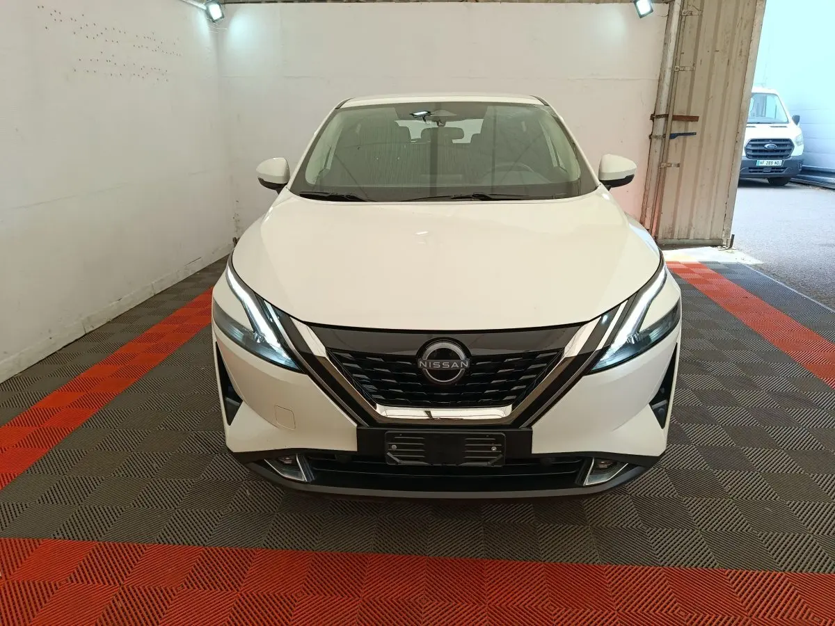 Vue frontale d'un Nissan Qashqai e-Power blanc, avec calandre noire et phares LED allumés, dans un garage.