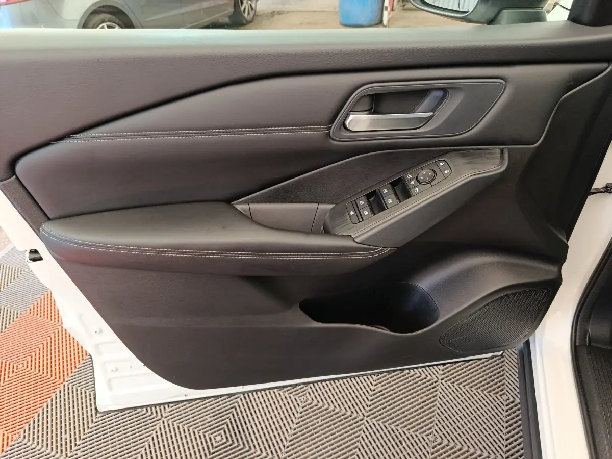 Vue intérieure côté gauche de la porte avant d’un Nissan Qashqai blanc, avec commandes électriques et accoudoir noir.