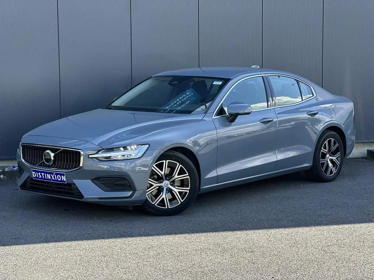 Volvo S60 gris Thunder en 3/4 avant droit, avec jantes alliage 17 pouces et contours de fenêtres chromés.