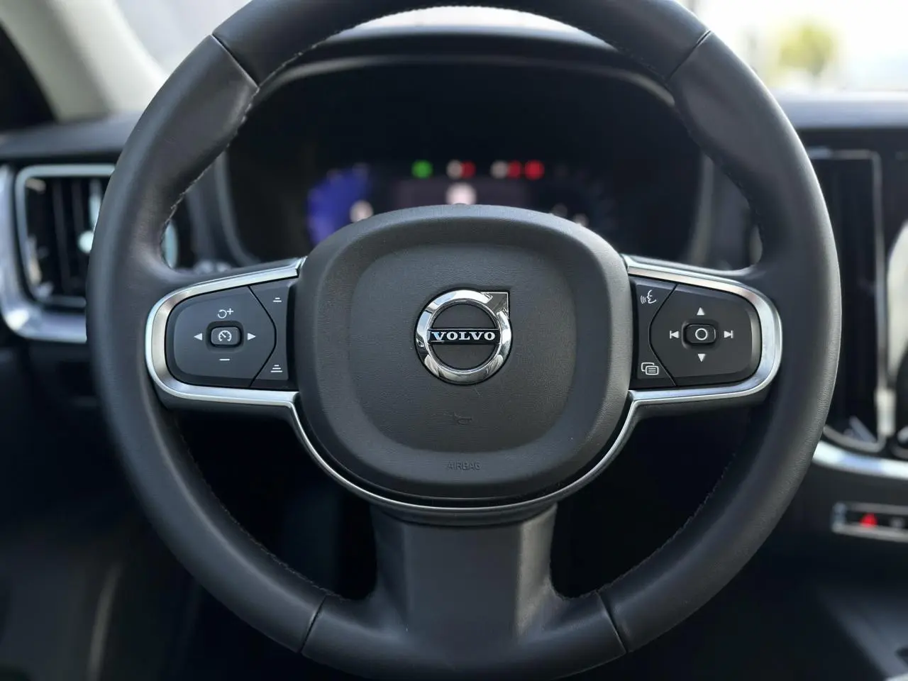 Gros plan sur le volant noir de la Volvo S60 2024 avec commandes intégrées et logo central chromé.