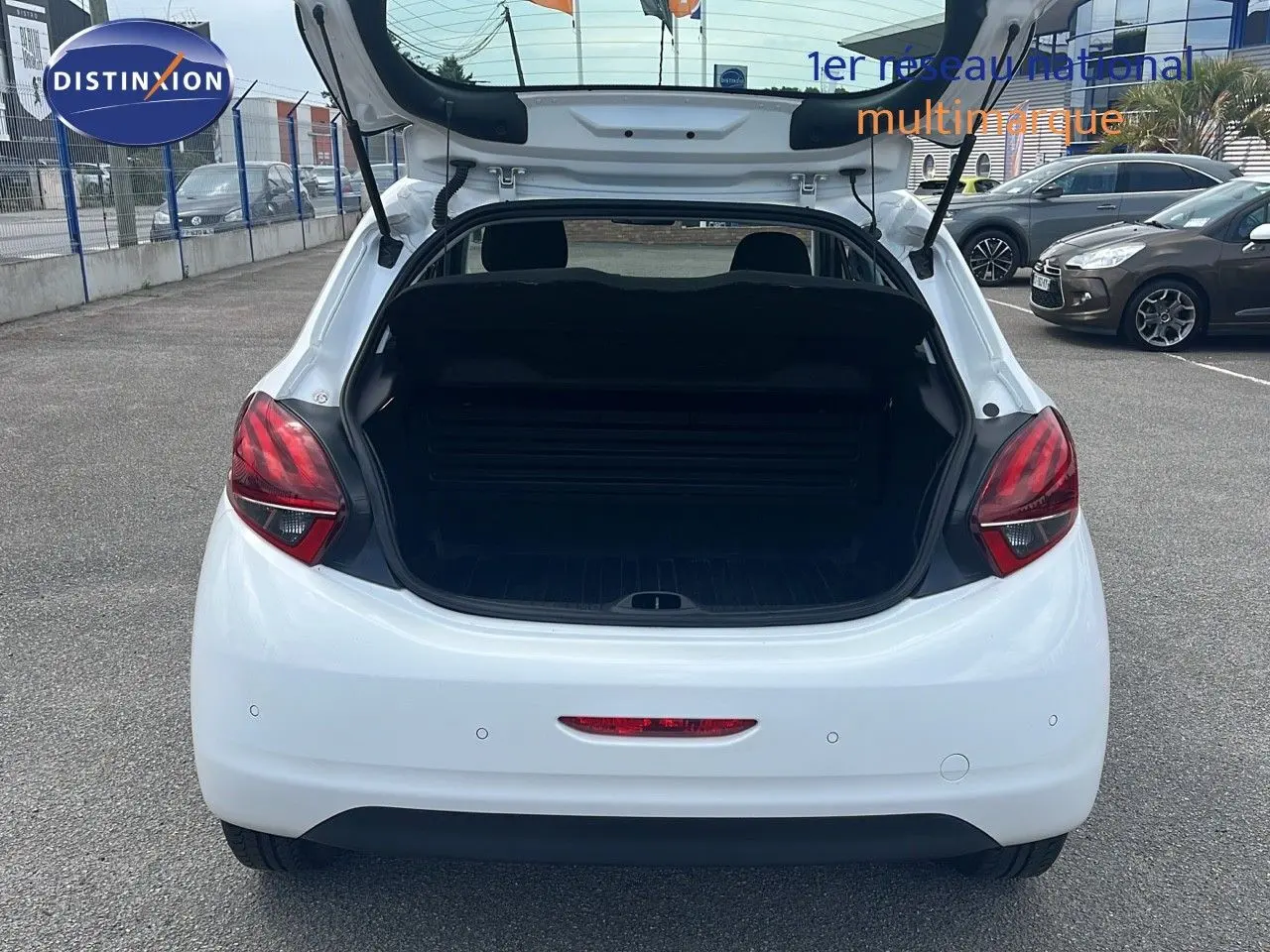 Vue arrière ouverte d'une Peugeot 208 blanche Banquise 2020, coffre dégagé et feux arrière rouges visibles.