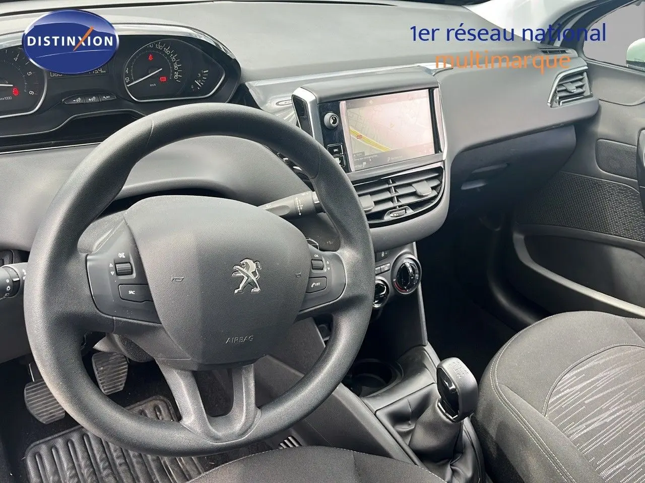 Vue intérieure du poste de conduite de la Peugeot 208 blanche, avec volant, tableau de bord et écran tactile central visibles.