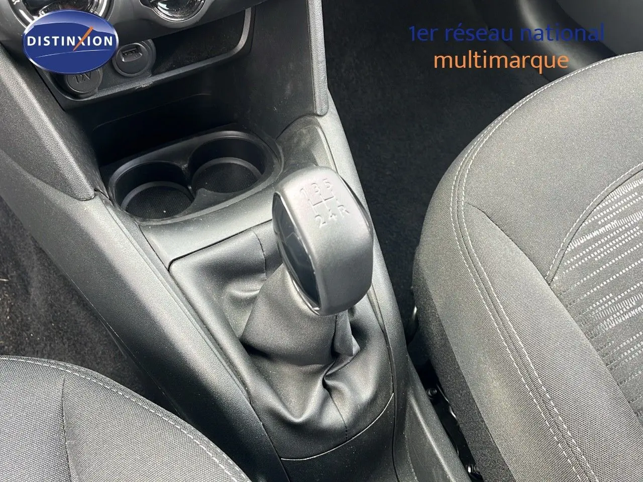 Gros plan sur la console centrale d'une Peugeot 208 blanche banquise, mettant en valeur le levier de vitesse manuel et les sièges noirs.