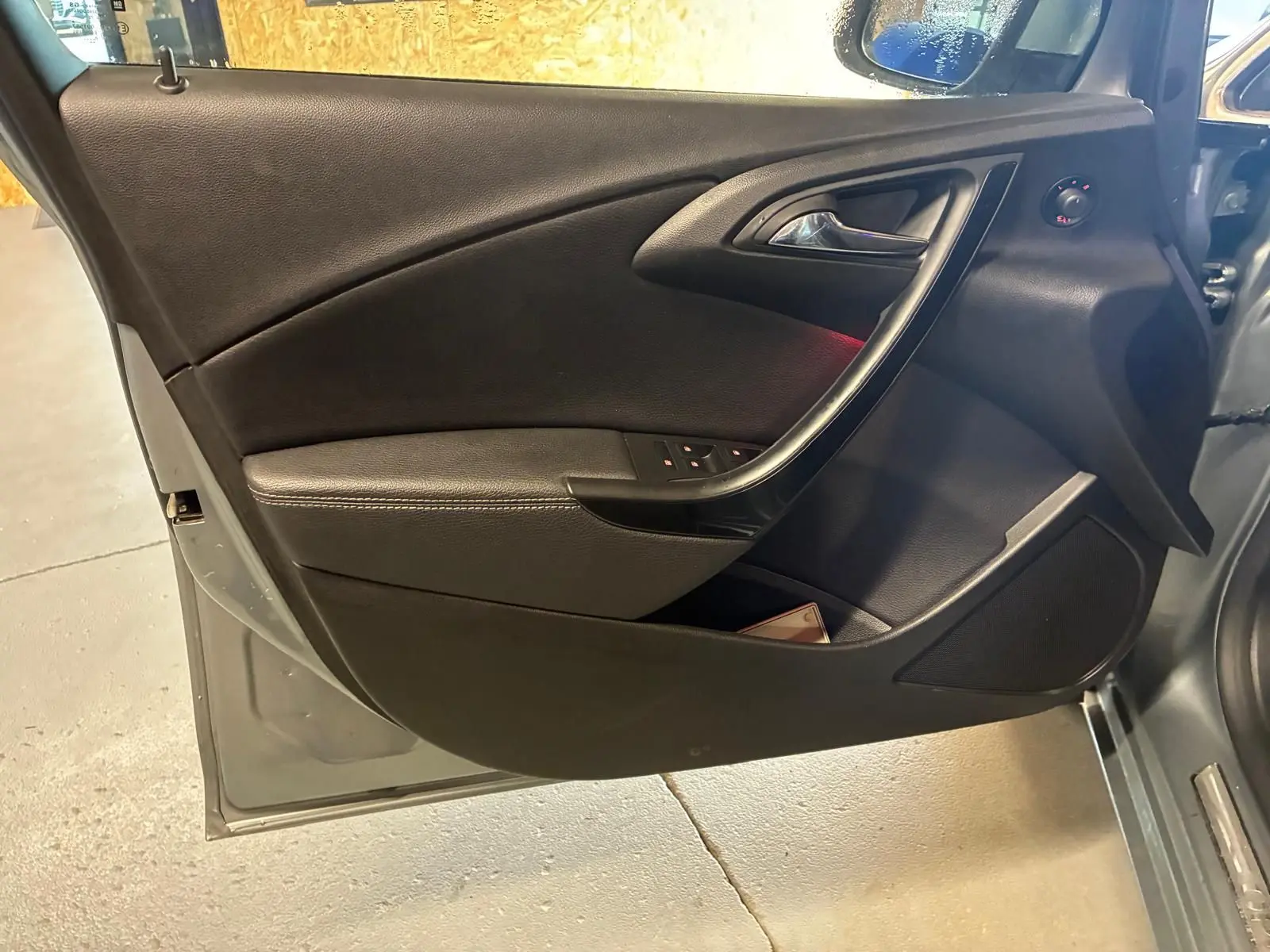 Vue intérieure côté gauche de la porte avant d’une Opel Astra gris 2015 avec garniture noire et commandes de vitres.