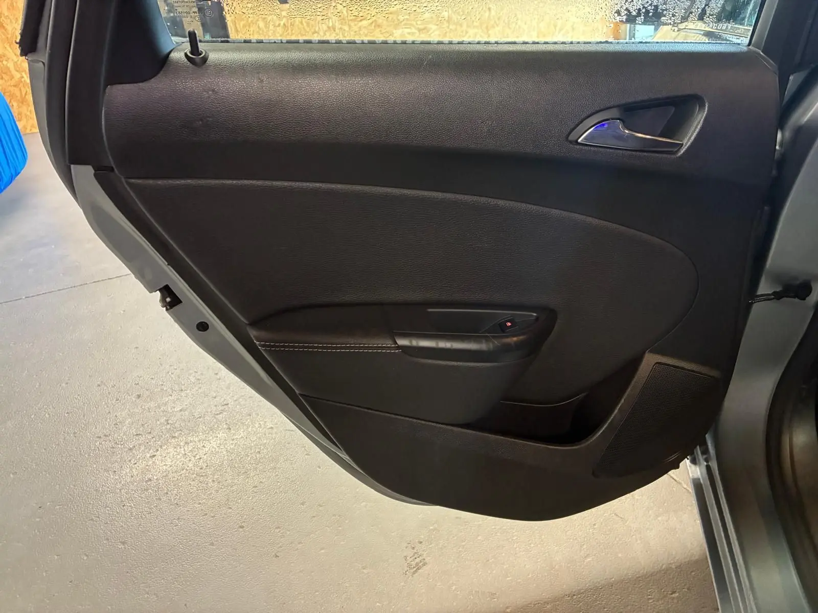 Vue intérieure de la porte arrière droite grise d'une Opel Astra 2015, avec poignée et commande de fenêtre noire.